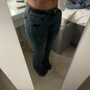 Mörkblå jeansbyxor från H&M - Säljer ett par lågmidjade mörkblå jeansbyxor från H&M med klassisk femficksdesign och raka ben. Jeansen har normal passform och är tillverkade i denim med orangea sömmar. Perfekta för dig som gillar en tidlös stil och snygg stil. Dessa är dessutom ALDRIG använda ute, då de endast är använda för att ta dessa bilder som syns i annonsen!!! Nyskick 