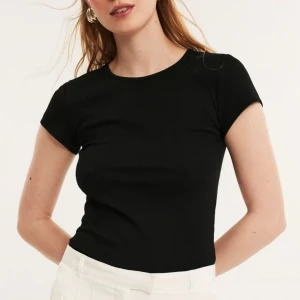 Svart ribbad t-shirt från Kappahl - En svart ribbad t-shirt från Kappahl med rund halsringning och korta ärmar. T-shirten har en tight passform och är tillverkad i mjuk bomull, perfekt för en enkel och stilren look.