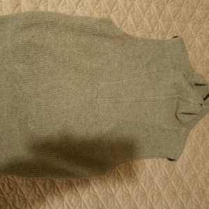 Grå stickad väst med dragkedja - Säljer en grå stickad väst med hög krage och dragkedja framtill. Västen har en ribbad struktur och är perfekt för lager-på-lager-stil. Passar både till jeans och kjol.