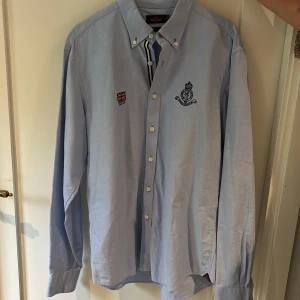 Ljusblå skjorta från Morris - Säljer en ljusblå skjorta från Morris med broderad logga på bröstet och en liten patch med brittisk flagga.  Nypris 1200 kr 