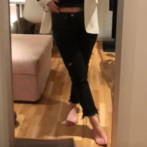 Svarta jeansbyxor med slitningar från Zara - Svarta jeansbyxor med slitna detaljer och råa benslut. Klassisk femficksmodell med dragkedja och knapp. Jeansen har en rak passform och är tillverkade i denim. Cropped rak modell
