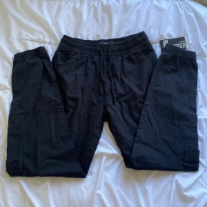  cargopants - Säljer ett par svarta cargopants med resår i midjan och snörning. Byxorna har stora fickor på sidorna och är perfekta för en avslappnad stil. Passar dig som gillar bekväma och praktiska byxor.
