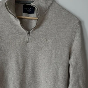 Beige stickad Bondelid kvarts zip - Säljer en beige stickad tröja från Bondelid med halv dragkedja vid halsen. Perfekt för lager-på-lager och stilren vardagslook.