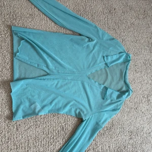Turkos mesh topp med v-ringning - Säljer en turkos långärmad mesh topp med djup v-ringning. Tunt och lätt material som passar perfekt för lager-på-lager eller som statement piece. Enkel och stilren design utan synliga detaljer.