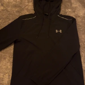 Under Armour Windbreaker - En windbreaker med reflex på axlarna och snören. Den är i nyskick, använd fåtal gånger. 