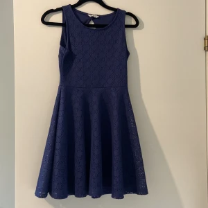 Blå ärmlös spetsklänning - Säljer en blå ärmlös klänning med rund hals och fint spetsmönster. Klänningen har en utställd kjol och en snygg öppen rygg. Perfekt för dig som vill ha en feminin och stilren look. Köpare betalar frakt!