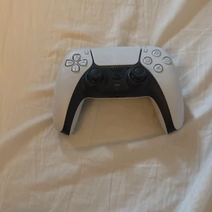 Ps5 kontroll - Bilderna visar en vit och svart spelkontroll, troligen till en spelkonsol. Ingen bok syns på bilderna, så ingen beskrivning av en bok kan ges.