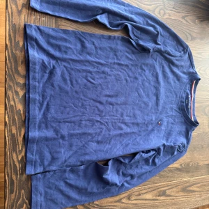 Blå långärmad tröja från Tommy Hilfiger - Säljer en klassisk blå långärmad tröja från Tommy Hilfiger. Tröjan har rund halsringning och en liten broderad logga på bröstet. Inga defekter och i ett mycket fint skick. Skriv till mig om ni har några frågor