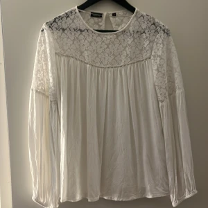 Långärmad blus med spets  - En långärmad vit blus med spets vid bröstet och ner till armarna samt fortsättande på ryggen. Storlek 40 men sitter som M. Luftig och skön. Skriv för fler bilder!