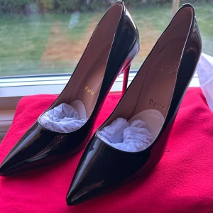 Svarta pumps från Christian Louboutin - Säljer ett par klassiska svarta pumps (helt nya) från Christian Louboutin med ikonisk röd sula. Skorna har spetsig tå och hög klack, tillverkade i glansigt skinn. Perfekta för dig som vill ha en tidlös och elegant look. Klackarna är 10cm. Priset kan diskuteras vid snabb affär.