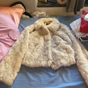 Beige pälsjacka från Vila - Säljer en supermjuk och fluffig beige pälsjacka från Vila i storlek S. Jackan har en klassisk krage och är helfodrad, perfekt för att hålla värmen under kyliga dagar. Snygg och trendig modell som lyfter vilken outfit som helst.
