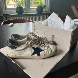 ÄKTA Golden Goose Superstar sneakers med blå stjärna - Säljer mina äkta Golden Goose då jag har haft de ett tag nu. Sjukt fina. Äktehetscertifikat följer med, köpta för ungefär 6000kr i golden goose butiken.    Har täckt över koden så att ingen annan kan använda min bild, skriv privat för fler bilder eller frågor! Skorna är storlek 40 men passar även 41-41.5. 