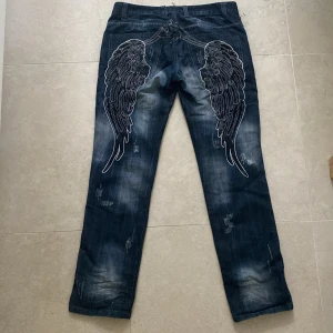 Svincoola jeans med vingar - Säljer dessa asscoola baggy mörkblå jeans från K & M jeans! De har ett par feta broderade vingar på rumpan, slitningar lite här och var och vita sömmar! Säljer de då de var lite för baggy på mig för min smak. Står att det är storlek 34 inuti jeansen, men skulle säga att det är som en M. Midja- 47cm.  Innerbenslängd- 86cm.  Ytterbensläng- 106cm. Bara att skriva vid frågor eller funderingar.💕