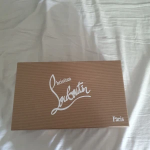Grå sneakers med nitar från Christian Louboutin - Säljer ett par gråa sneakers från Christian Louboutin med coola nitar på tån och sidorna. Skorna har snörning och är tillverkade i mocka med detaljer i skinn. Perfekta för dig som vill sticka ut med en lyxig och Stockholm stil