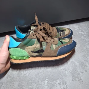 Valentino rock runner  - Säljer ett par Valentino Rockrunner sneakers med militärtema – ett perfekt tillskott till garderoben för dig som vill kombinera lyx och edge! Skorna har en snygg camo-design i dova, jordnära toner med Valentino’s signaturdetaljer och bekväm passform som gör dem lika stiliga som praktiska. Kolla gärna in mina andra annonser – jag säljer fler märkesplagg och accessoarer, och jag erbjuder bra bundle-deals vid köp av flera produkter. Passa på att fynda. Nypris: 6000kr. Skorna har inga innersulor