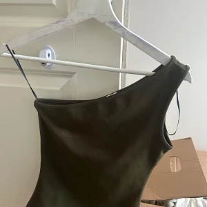 One shoulder topp - Snygg olivgrön topp med one shoulder-design och smal axelrem. Perfekt för dig som vill ha en trendig och stilren look. Tunt och mjukt material som sitter skönt mot kroppen.