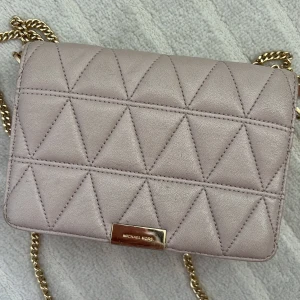 Rosa/nude quiltad axelväska från Michael Kors - Säljer en stilren nude/ljus rosa axelväska från Michael Kors med quiltat mönster och guldfärgad kedja. Väskan har en metallplatta framtill med logga och stängs med magnetlås. 