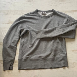 Grå sweatshirt från Acne Studios - Säljer en stilren grå sweatshirt från Acne Studios med rund halsringning och diskret logga tryckt framtill. Tröjan har långa ärmar och är tillverkad i mjuk bomull, perfekt för en avslappnad look. Skickar dagen efter du köper!