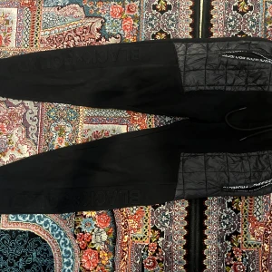 Svarta mjukisbyxor från Black Squad - Svarta mjukisbyxor från Black Squad med tryckt logga på benet och quiltade detaljer vid fickorna. Byxorna har dragsko i midjan och är tillverkade i mjukt material, perfekta för en avslappnad stil.