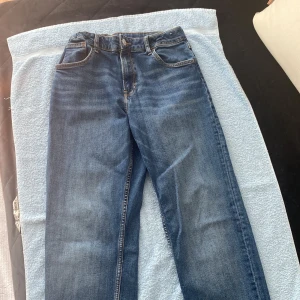 Blå jeans med relaxed fit från H&M - Tja jag Säljer ett par klassiska blå jeans från H&M med relaxed fit och tapered leg. Jeansen har justerbar midja, fem fickor och normal passform. Perfekta för en avslappnad stil och passar till det mesta.