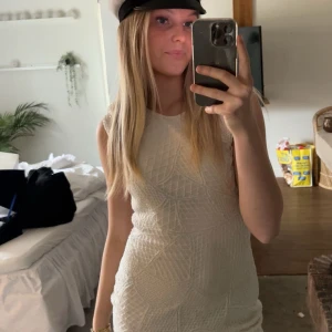 Vit klänning  - Säljer en vit kortklänning från Rebecca Stella med glittrigt mönster och ärmlös design. Klänningen har rund halsringning och figurnära passform, perfekt för student eller sommarens festligheter.