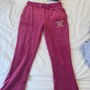 Rosa mjukisbyxor från Juicy Couture - Säljer ett par rosa mjukisbyxor från Juicy Couture med dragsko i midjan och två bakfickor. Byxorna har ett glittrigt Juicy Couture-logo framtill och är i mjukt, skönt material! Har använts förut men den är inte sönder någonstans som jag har märkt. Barnstorlek 134