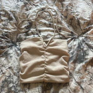 Beige croppad linnetopp med knytband - Säljer en beige croppad linnetopp med smala knytband och rynkdetalj framtill. Perfekt för varma dagar och enkel att styla med jeans eller kjol.