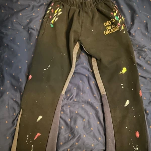 Svarta mjukisbyxor från Gallery Dept. - Svarta mjukisbyxor från Gallery Dept. med färgstänk i gult, rött, grönt och vitt. Byxorna har resår i midjan och tryckt text på ena höften. Tillverkade i 100% bomull och har en avslappnad passform med kontrastpaneler längs benen. Priset är ej hugget i sten och skriv vid minsta fundering🔥