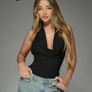 Svart halterneck topp - Snygg svart halterneck topp med djup urringning och draperad framsida. Perfekt att styla med jeans eller kjol för en trendig look. Toppens material ser ut att vara mjukt och följsamt.
