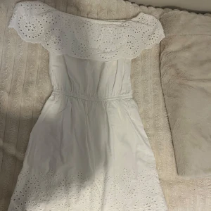 Vit offshoulder klänning från BikBok - Superfin vit klänning från BikBok med offshoulder-modell och broderade spetsdetaljer. Klänningen har resår i midjan och vackra hålbroderier längs volangen och nederkanten. Perfekt för sommarens alla tillfällen!