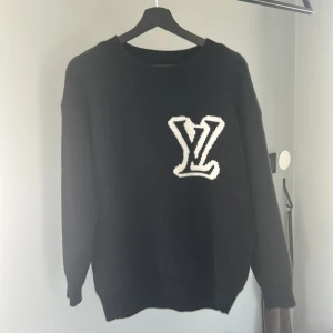 Svart stickad tröja från Louis Vuitton - Säljer en svart stickad tröja från Louis Vuitton med stort vitt LV-logo på bröstet. Tröjan har rund halsringning och långa ärmar. Perfekt för dig som gillar exklusiva och stilrena plagg.