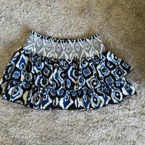 Mönstrad volangkjol från Francis - Kort volangkjol med blått, svart och vitt mönster från Francis. Kjolen har bred resår i midjan med ett stickat mönster och två lager volanger. Skulle säga att den är lågmidjade men om man tycker den är för lång kan man även vika ner resåren💗 