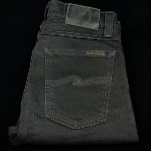 Svarta jeans från Nudie Jeans - Säljer ett par svarta jeans från Nudie Jeans med klassisk femficksdesign och diskreta sömmar på bakfickorna. Jeansen har normal passform och är tillverkade i ett slitstarkt denimtyg. Perfekta för dig som gillar stilrena och tidlösa byxor.