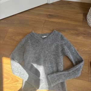 Grå stickad tröja från Cubus - Mysig grå stickad tröja från Cubus med v-ringad hals. Tröjan har lång ärm och är tillverkad i ett stickat material som passar perfekt för kyligare dagar. Enkel och stilren design som är lätt att matcha.