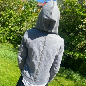 long zipper zip-hoodie - Enkel grå kofta me nice detalj. Långa fungerande dragkedjor i rygg och på framsida. Den går även att bära med kluven luva. En lagad skada på arm men som i min åsikt ger extra detalj på plagget. 