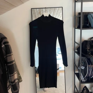 Svart långärmad klänning med polokrage - En stilren svart klänning med lång ärm och polokrage. Klänningen har en tight passform och är knälång, perfekt för dig som gillar en minimalistisk look. Passar lika bra till sneakers som boots.