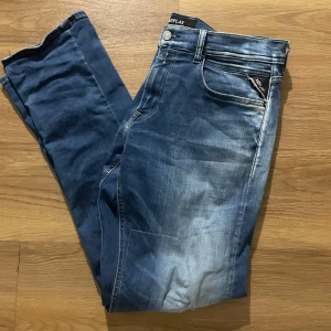 Replay Grover jeans - Säljer ett par Replay Grover jeans i klassisk blå tvätt med slitningar och lagade detaljer på benen. Jeansen har normal passform, dragkedja och femficksdesign. Perfekta för dig som gillar en avslappnad och trendig stil. Storleken är 33/32!