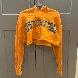 Orange croppad hoodie från STAY - Säljer en orange croppad hoodie från STAY med texten 'DISTORTION' i svart och vitt på bröstet. I strl L men sitter snyggt på både S o M