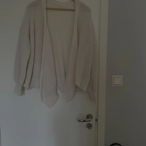 Beige stickad kofta - Mysig beige stickad kofta med lång ärm och avslappnad passform. Perfekt att slänga på sig över en t-shirt eller topp för extra värme. Enkel och stilren design utan knappar eller dragkedja.