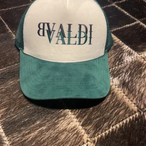 Grön och vit keps från BVALDI - Snygg keps från BVALDI i grön och vit färg. Framsidan är vit med broderad logga i svart och grön, medan baksidan är i grönt meshmaterial för bra ventilation. Justerbar storlek med plastspänne bak.