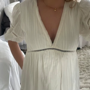 Vit kortklänning med spetsdetaljer - Supersöt vit kortklänning med v-ringning, balong ärmar och spetsdetaljer. Är i storlek s men ser större ut då ja har för mig att de är en oversize modell.