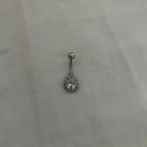 Navelpiercing med glittrande stenar - Säljer en snygg navelpiercing i silverfärg med en droppformad design. Smycket är i titan och perfekt för dig som vill ha något extra till din look! Köpt för 150 och endast använt en gång💞