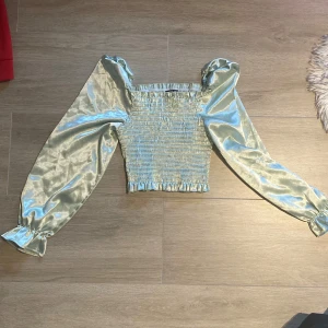 Ljusgrön satinblus med puffärmar från SHEIN - Trendig ljusgrön blus i satin från SHEIN med smockad kropp och långa puffärmar. Toppen har en croppad passform och resår vid ärmslut och axlar för extra volym. Perfekt för dig som vill sticka ut med en glansig look.