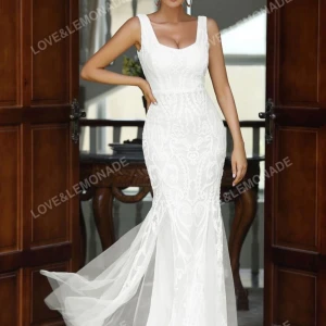 Vit långklänning från Love&Lemonade - Elegant vit långklänning med djup v-ringning och breda axelband. Klänningen har figurnära passform och vackert mönstrad spets över hela plagget samt lätt utsvängd nederdel med släp.