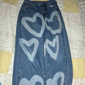 Blå jeans med hjärtmönster -  Lite slitna vid kanten/hålet vid fötterna.
