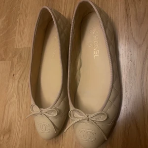 Beige ballerinaskor från Chanel - Snygga beige ballerinaskor från Chanel med quiltad design och rosett framtill. Skorna har rund tå och är tillverkade i skinn med diskret Chanel-logga broderad på tån. Fick dessa av mamma när hon rensade sin garderob, har tyvärr inte kvar boxen eller dustbag då hon har mycket märkessaker. Tyvärr små i storleken därför har vi inte kunnat ha dom, passar en 39. 