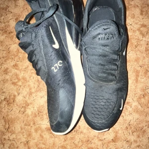 Nike Air Max 270 svarta sneakers - Svarta Nike Air Max 270 sneakers med vit och orange sula. Skorna har snörning, rund tå och synlig Air Max-dämpning på hälen. Snygg sportig design med diskreta vita detaljer och meshmaterial för bra andningsförmåga. Säljs för att den ej passa min stil 