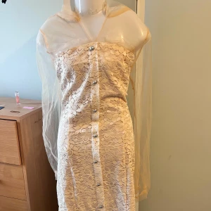 Ljus pink  spetsklänning med knappar - Elegant  klänning i spets med knappar framtill. Den har långa ärmar i transparent material och en kort längd. Perfekt för en stilfull look.