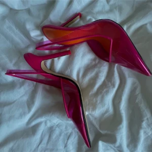 Rosa pumps med spetsig tå från Zara - Snygga pumps i transparent rosa plast med spetsig tå och hög klack. Skorna har en orange innersula och smal rem runt hälen för en modern vibe. Perfekta för dig som vill sticka ut med färg och form.