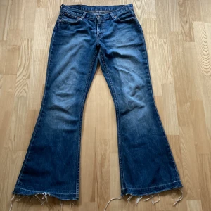 Levis Flare jeans  - Säljer ett par klassiska blå Levi's jeans med bootcut och rå, fransig kant nertill. Jeansen har fem fickor, normal passform och är tillverkade i slitstarkt denim. Perfekta för dig som gillar en retro och avslappnad look.